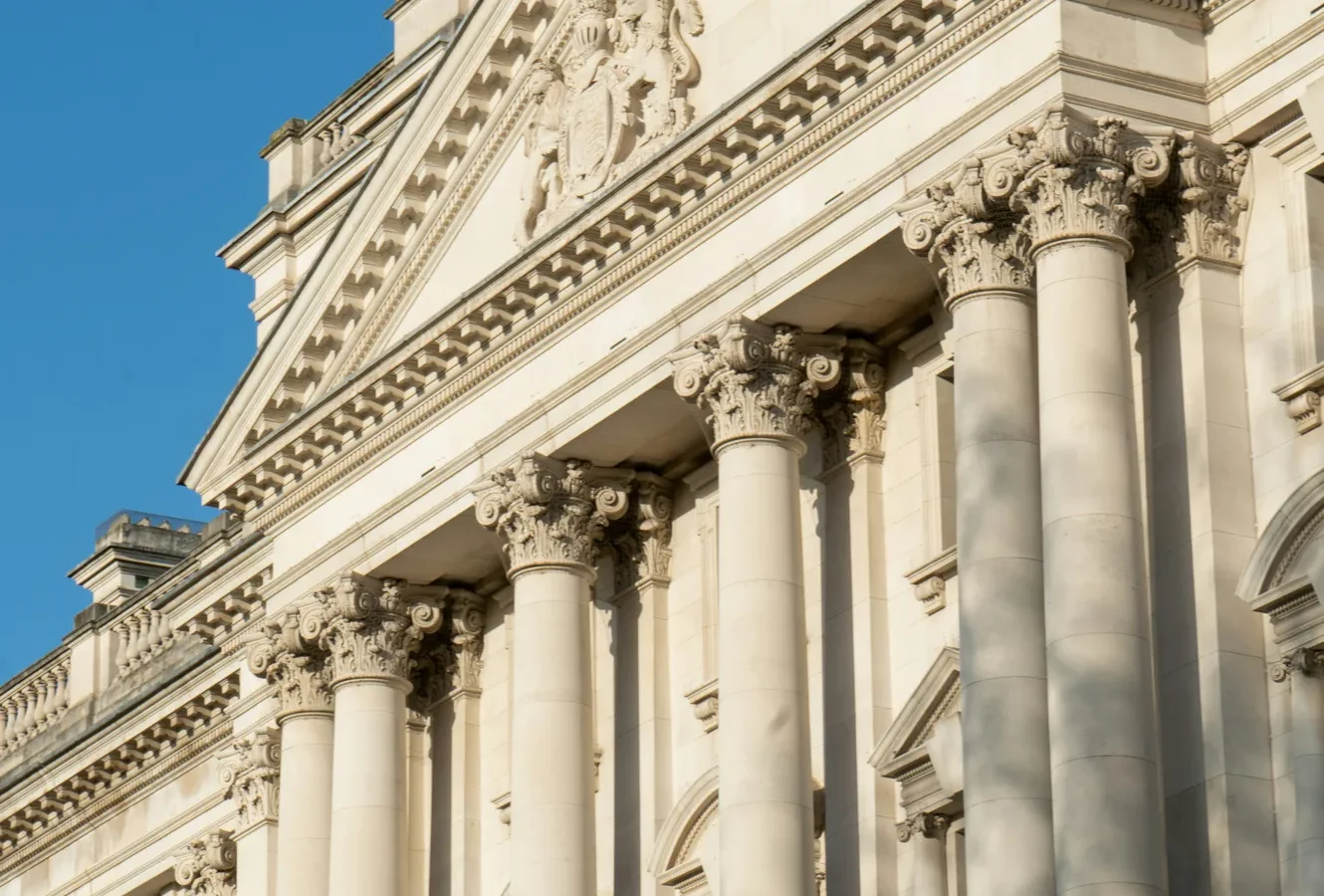 Classical neoclassical building facade with white stone columns, ornate Corinthian capitals, and decorative entablature against clear blue sky.