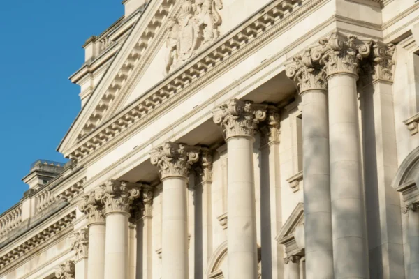 Classical neoclassical building facade with white stone columns, ornate Corinthian capitals, and decorative entablature against clear blue sky.
