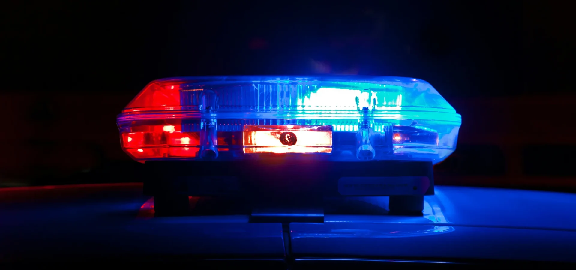Emergency vehicle light bar with red lights on left, white center display, and blue lights on right, illuminated against dark background.