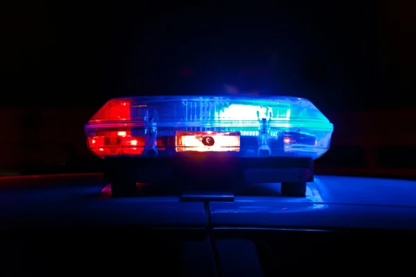 Emergency vehicle light bar with red lights on left, white center display, and blue lights on right, illuminated against dark background.