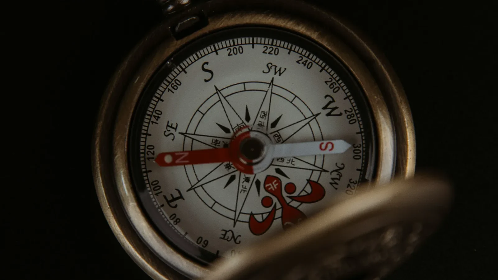 Antique brass compass with red needle and cardinal directions marked on white face against black background.